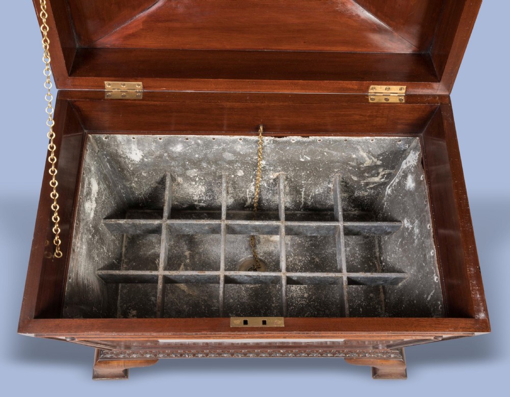 A sarcophagus-shaped antique mahogany wine cooler with carved decorative borders, side brass carrying handles, and brass castors. View IV