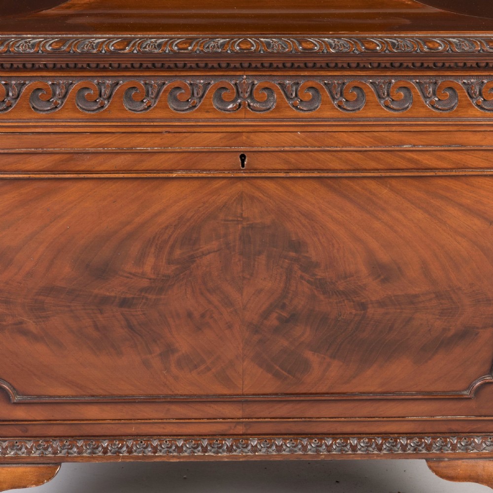 A sarcophagus-shaped antique mahogany wine cooler with carved decorative borders, side brass carrying handles, and brass castors. View V