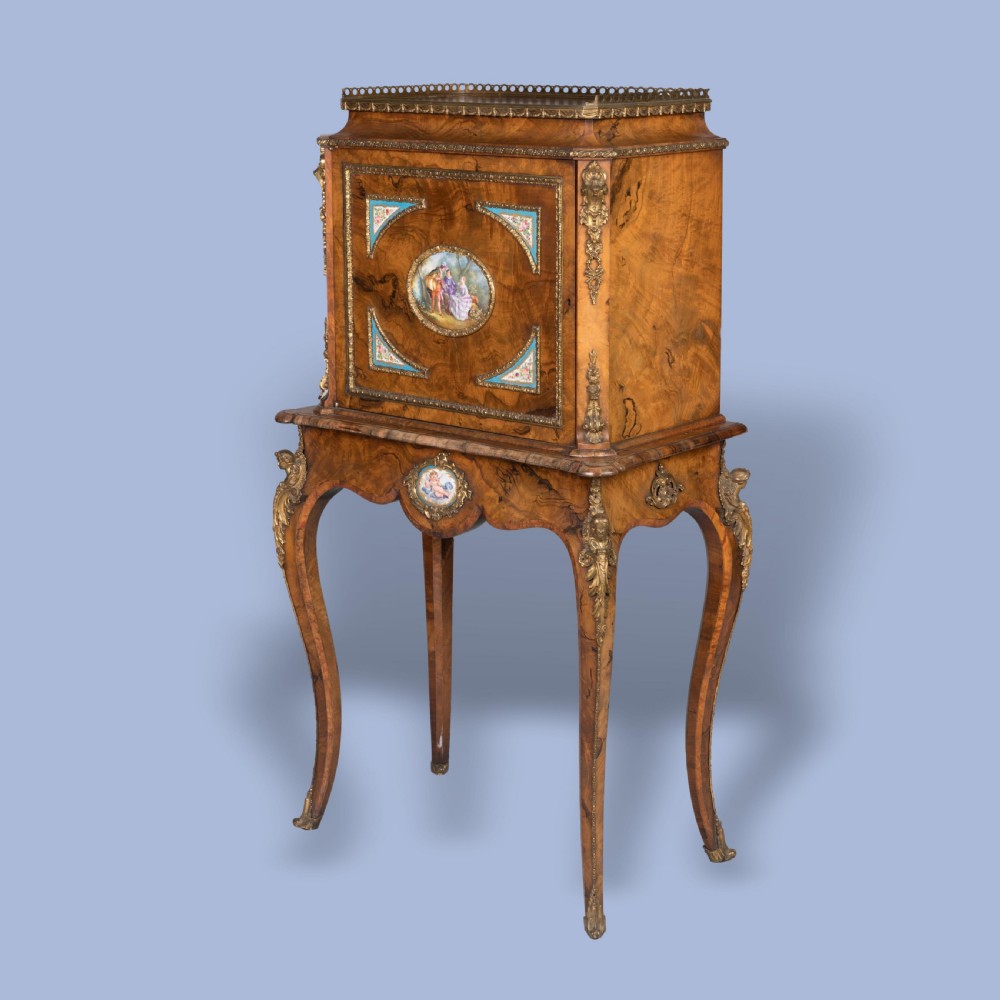 An English burr walnut cabinet on stand featuring cabriole legs, gilt-bronze mounts, a brass top gallery, and inset porcelain plaques.