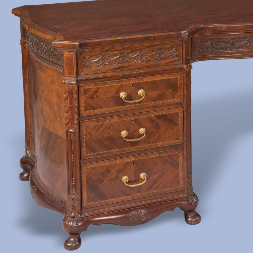 An antique mahogany pedestal desk featuring a serpentine front, parquetry drawer fronts, brass handles, and carved blind fretwork along the frieze. View V