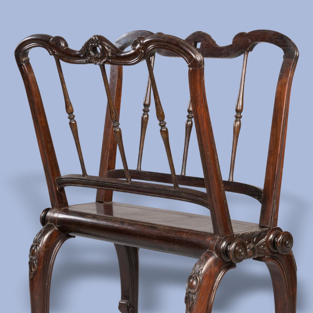 A late Georgian dark mahogany folio stand featuring carved slatted side supports, turned spindles, curved legs, and small brass castors. View II