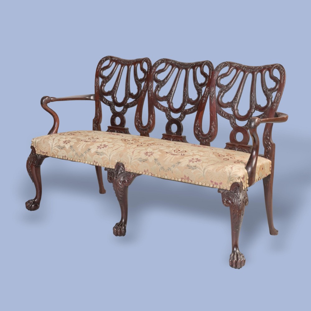 A George II style triple-back carved mahogany settee featuring intricate pierced splats, floral fabric upholstery, and cabriole legs with ball-and-claw feet.