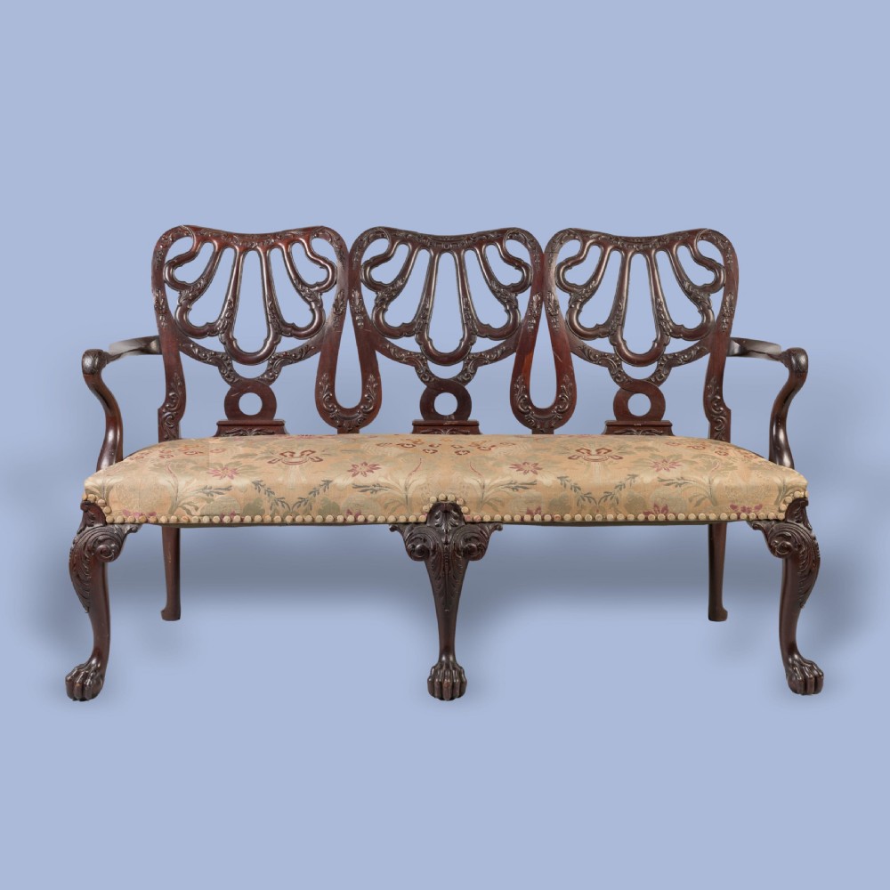 A George II style triple-back carved mahogany settee featuring intricate pierced splats, floral fabric upholstery, and cabriole legs with ball-and-claw feet. View V