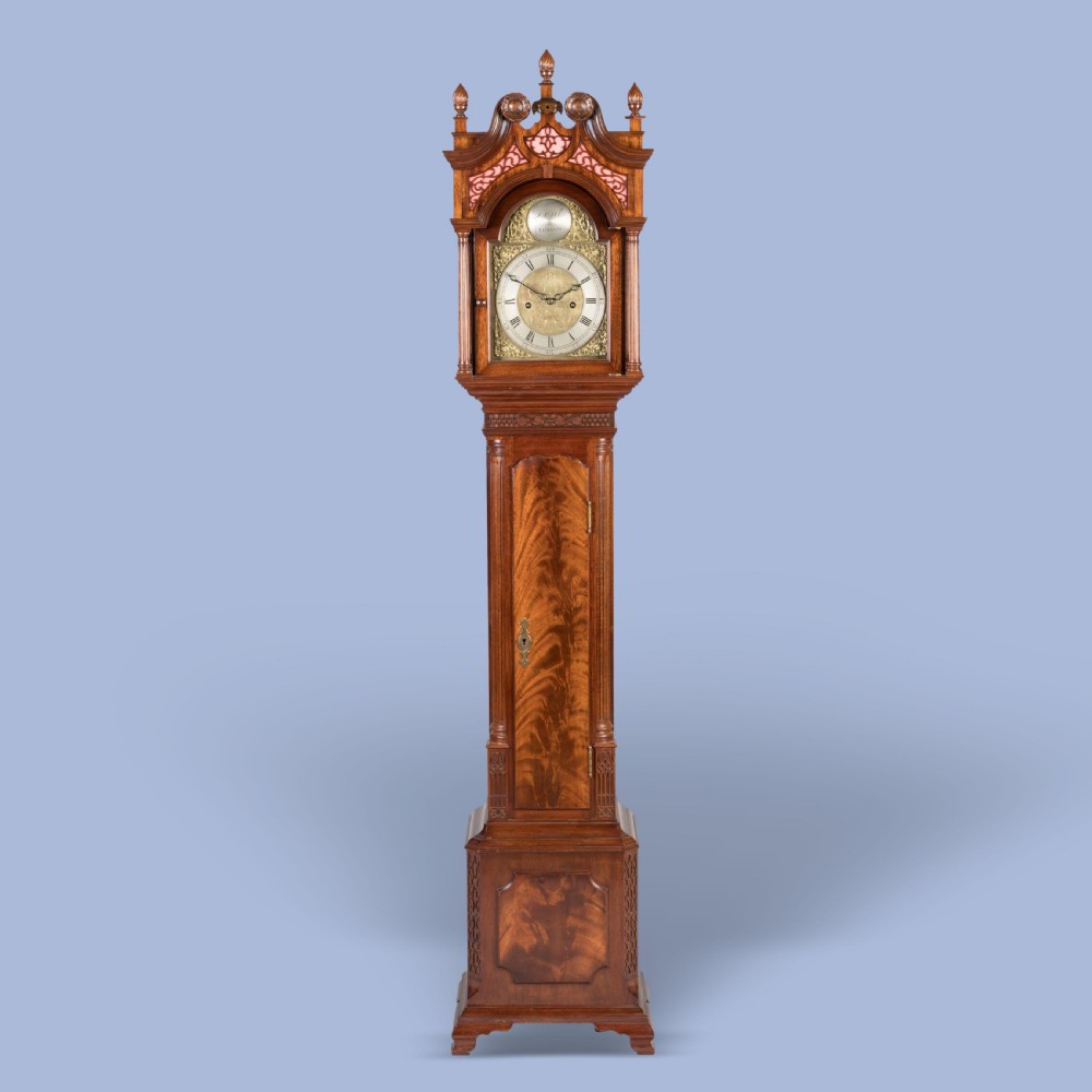 A miniature mahogany longcase clock featuring a brass dial, swan-neck pediment with brass finials, and a flame mahogany veneer trunk door. View II