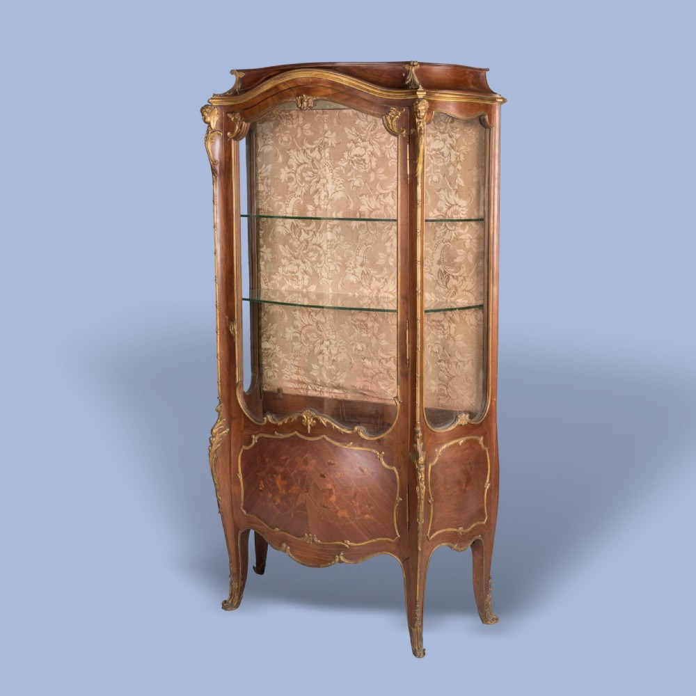 A French Transitional style bombe vitrine featuring curved glazed sides, floral marquetry panels, cabriole legs, and ornate gilt-bronze mounts.