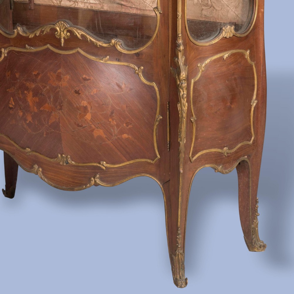 A French Transitional style bombe vitrine featuring curved glazed sides, floral marquetry panels, cabriole legs, and ornate gilt-bronze mounts. View II