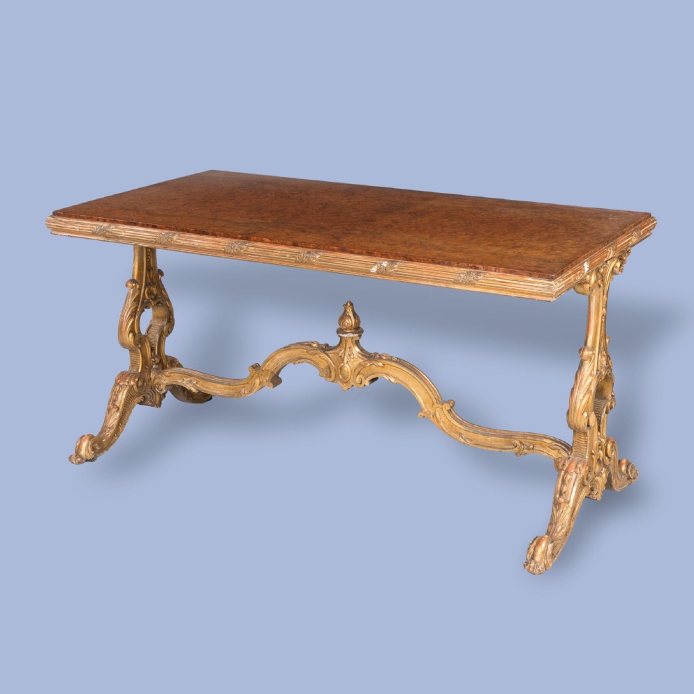 A mid-19th century rectangular centre table with a figured amboyna wood top set over a carved giltwood trestle base featuring a central finial.