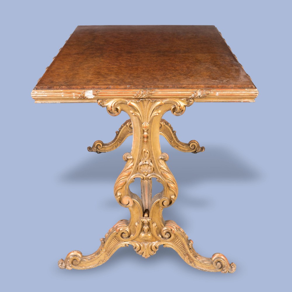A mid-19th century rectangular centre table with a figured amboyna wood top set over a carved giltwood trestle base featuring a central finial. View IV