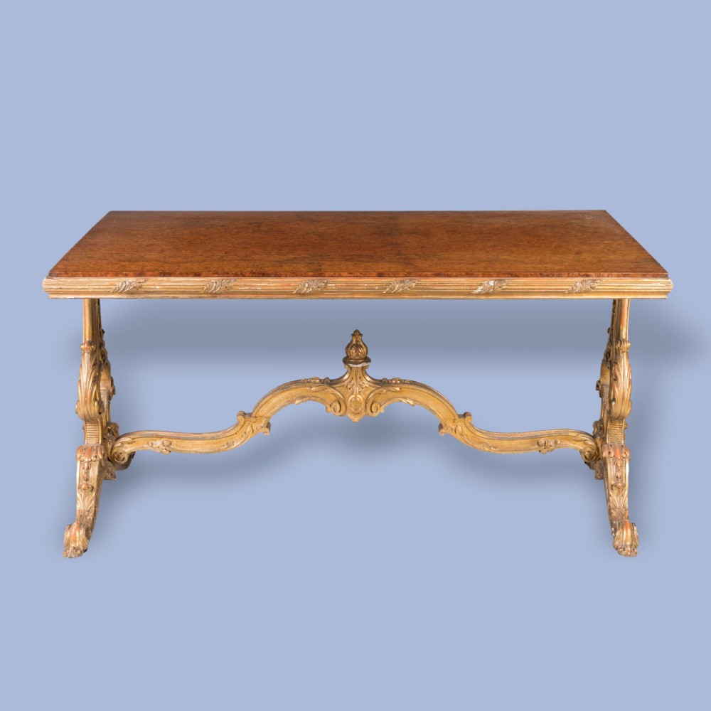 A mid-19th century rectangular centre table with a figured amboyna wood top set over a carved giltwood trestle base featuring a central finial. View VI