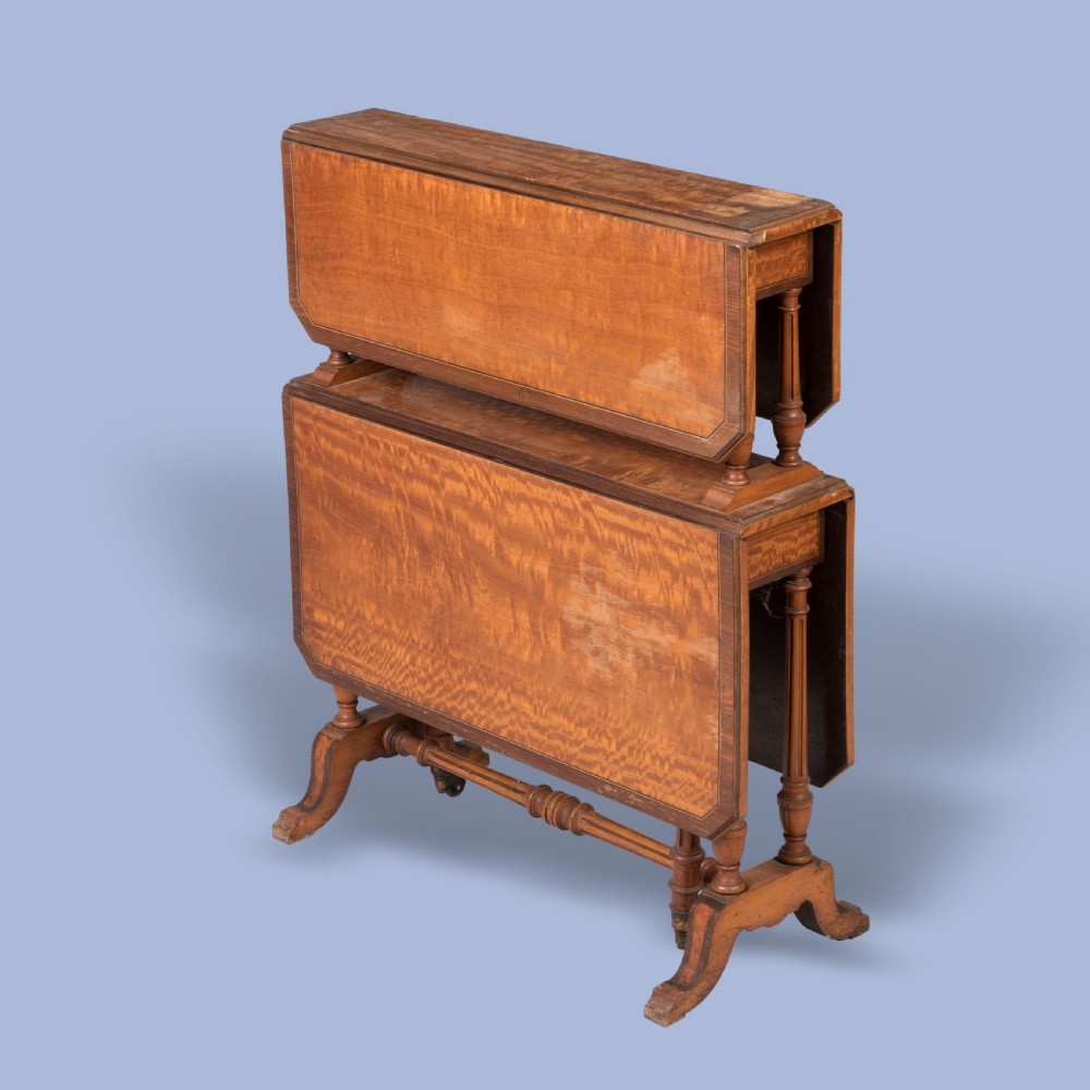 A double-tiered satinwood Sutherland drop-leaf table featuring turned leg supports, crossbanded borders, and brass castors. View II