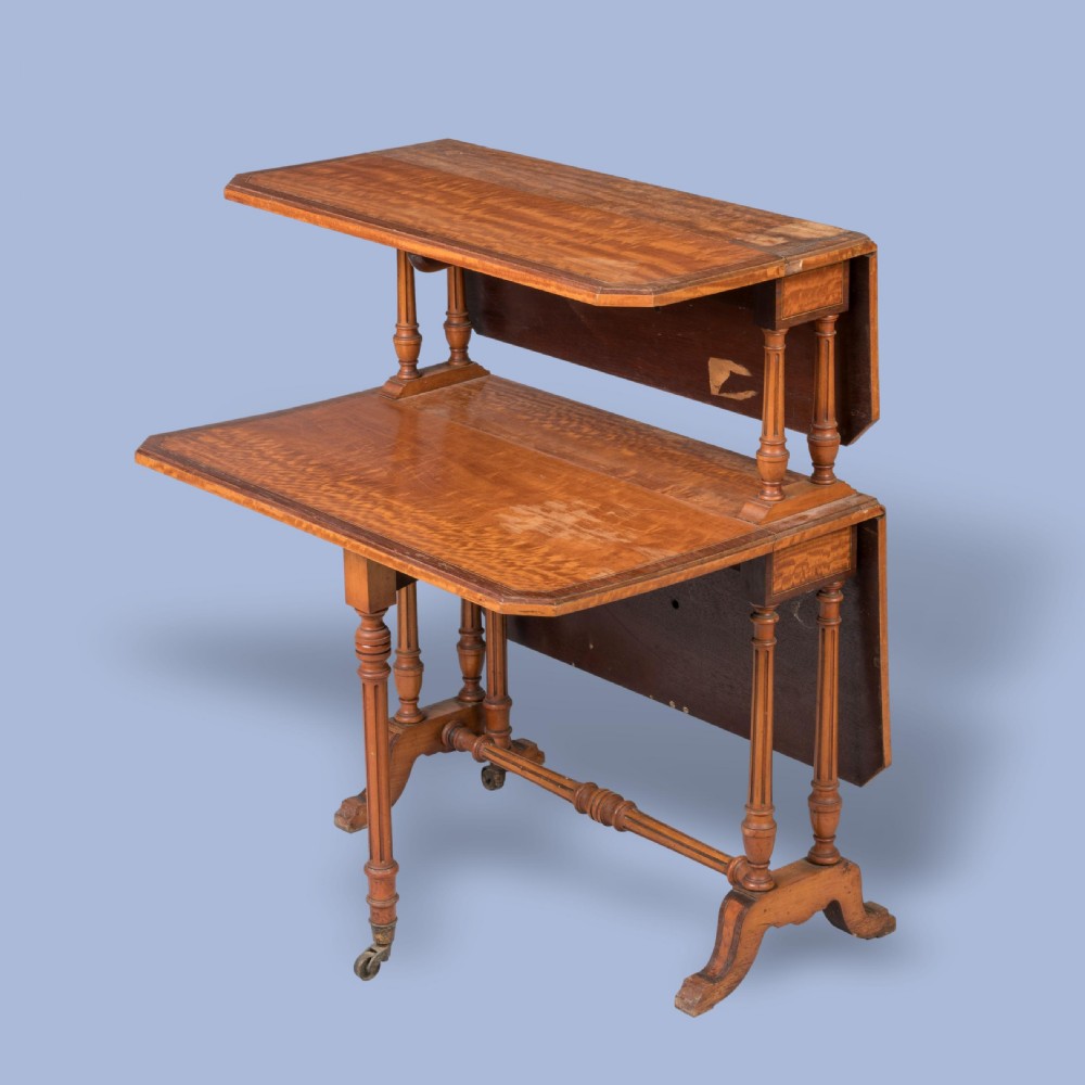 A double-tiered satinwood Sutherland drop-leaf table featuring turned leg supports, crossbanded borders, and brass castors. View III
