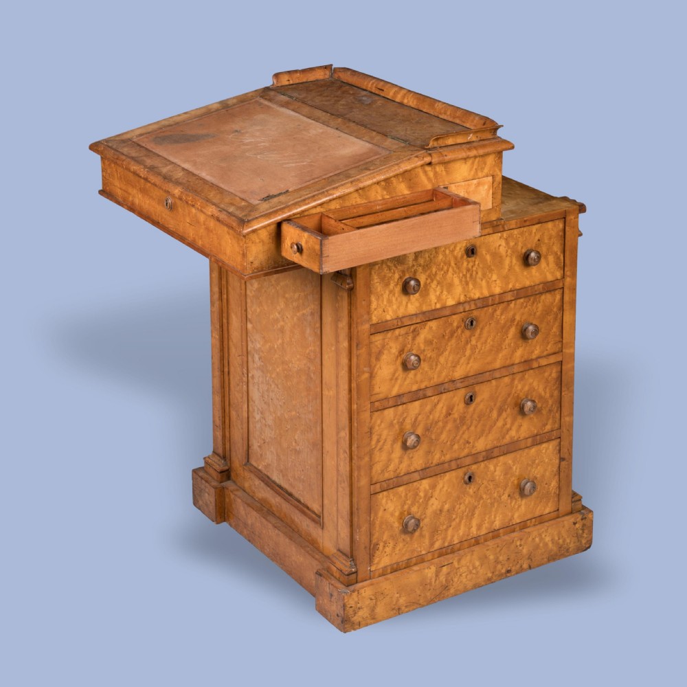 A late Georgian davenport desk crafted from golden timber with a sliding slanted leather writing top, side drawers with turned wooden knobs, and an extended side pen drawer.