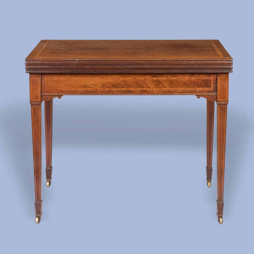 An Edwardian inlaid mahogany games table with square tapered legs, brass castors, and satinwood stringing.