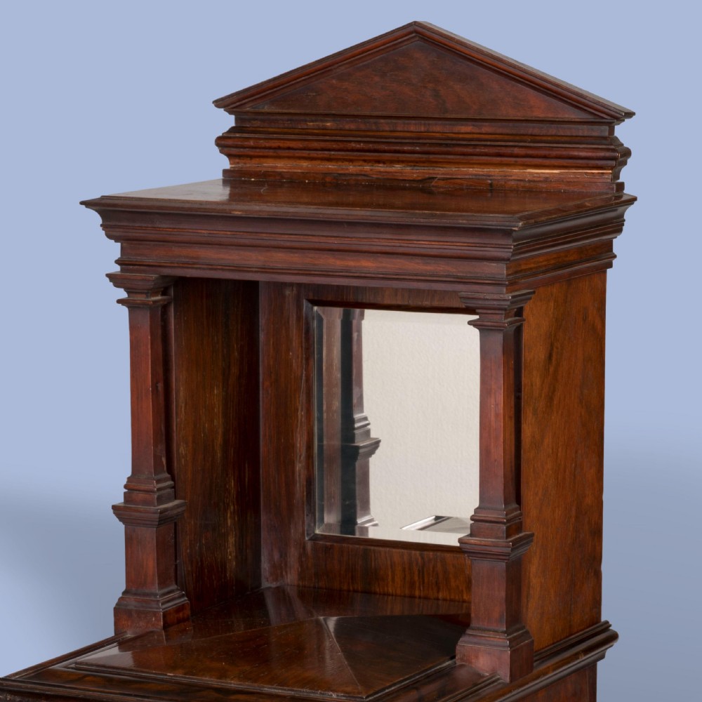 A dark mahogany Victorian music cabinet featuring a pedimented top, an upper section with open horizontal shelves, a glazed lower door, a brass presentation plaque, and small castors at the base. View V