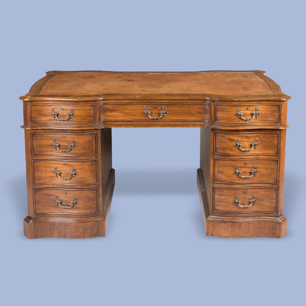 A George III style mahogany pedestal library desk featuring a leather writing surface, serpentine contoured front, nine drawers, and brass bail handles. View II