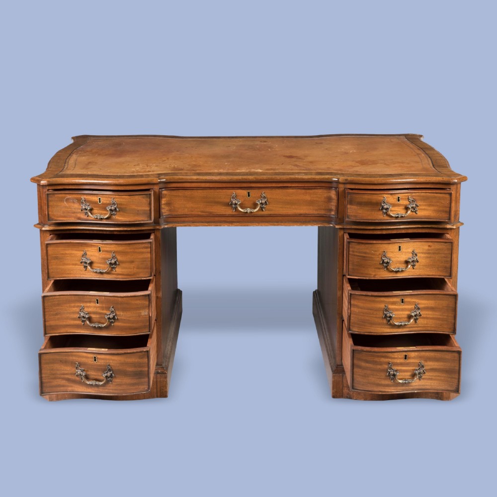 A George III style mahogany pedestal library desk featuring a leather writing surface, serpentine contoured front, nine drawers, and brass bail handles. View III
