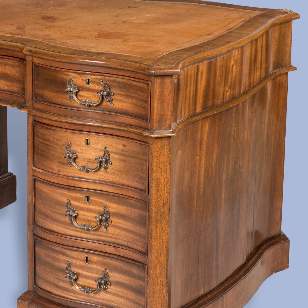 A George III style mahogany pedestal library desk featuring a leather writing surface, serpentine contoured front, nine drawers, and brass bail handles. View IV