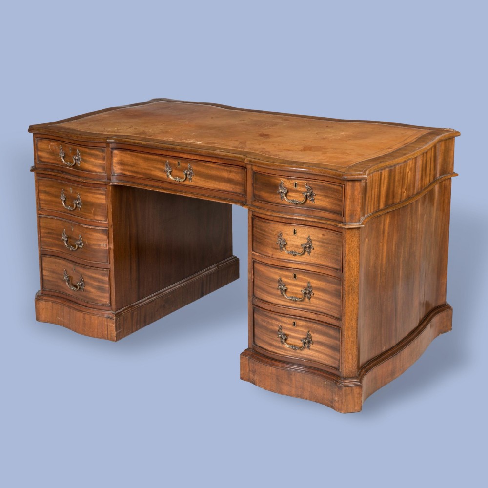 A George III style mahogany pedestal library desk featuring a leather writing surface, serpentine contoured front, nine drawers, and brass bail handles. View V