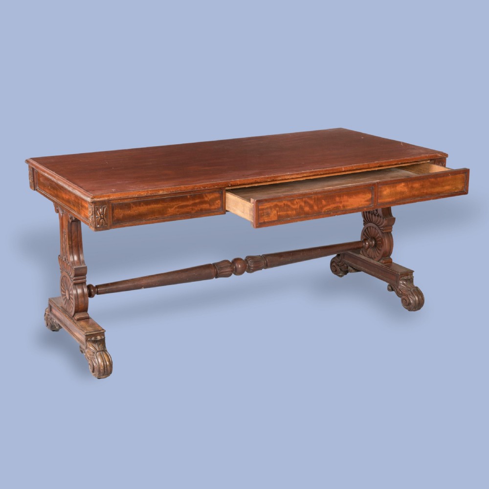 A Regency mahogany library table featuring a flat rectangular top, three frieze drawers, carved trestle end supports, and a central turned stretcher. View II