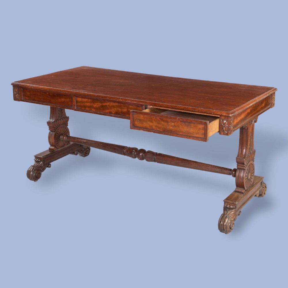A Regency mahogany library table featuring a flat rectangular top, three frieze drawers, carved trestle end supports, and a central turned stretcher. View III