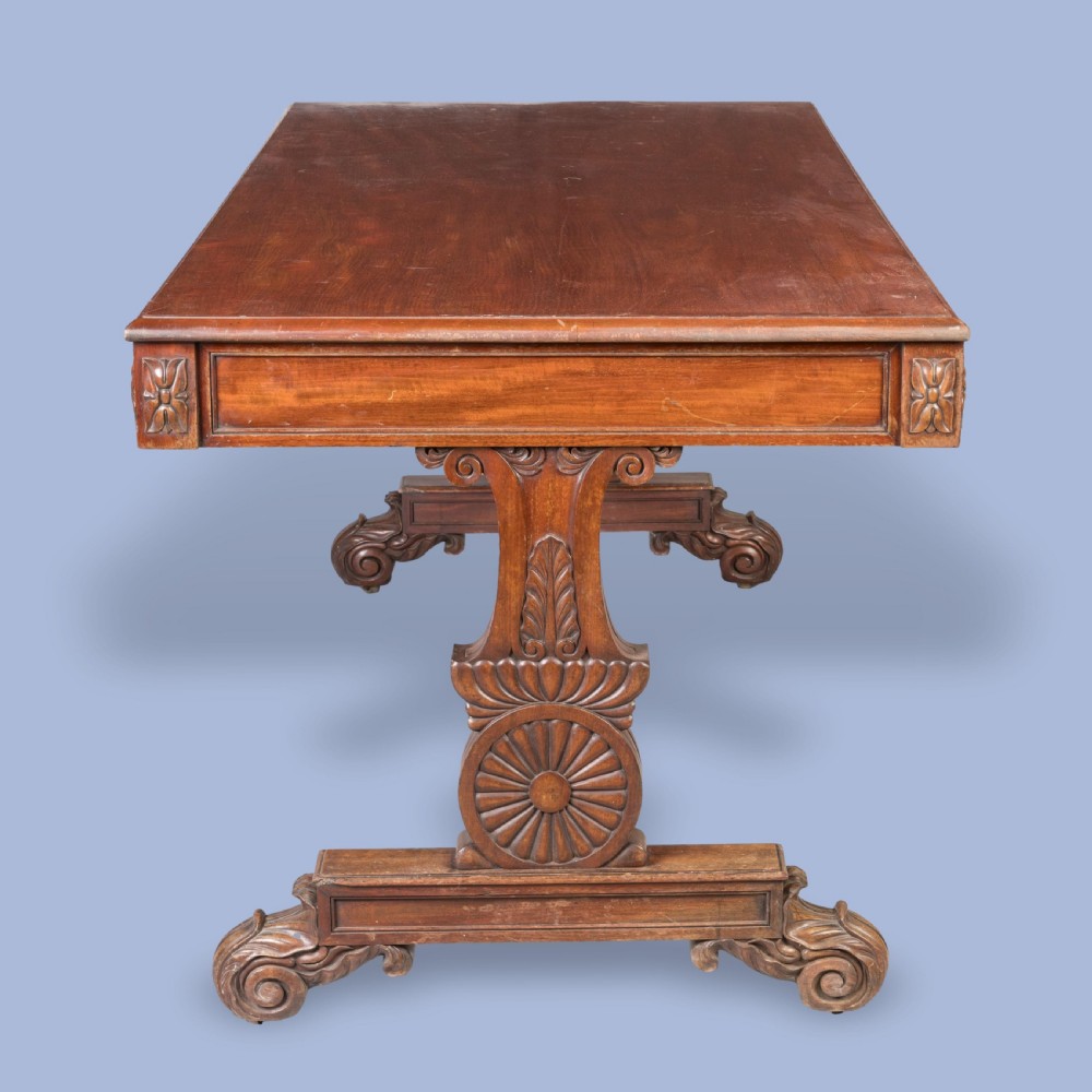 A Regency mahogany library table featuring a flat rectangular top, three frieze drawers, carved trestle end supports, and a central turned stretcher. View V