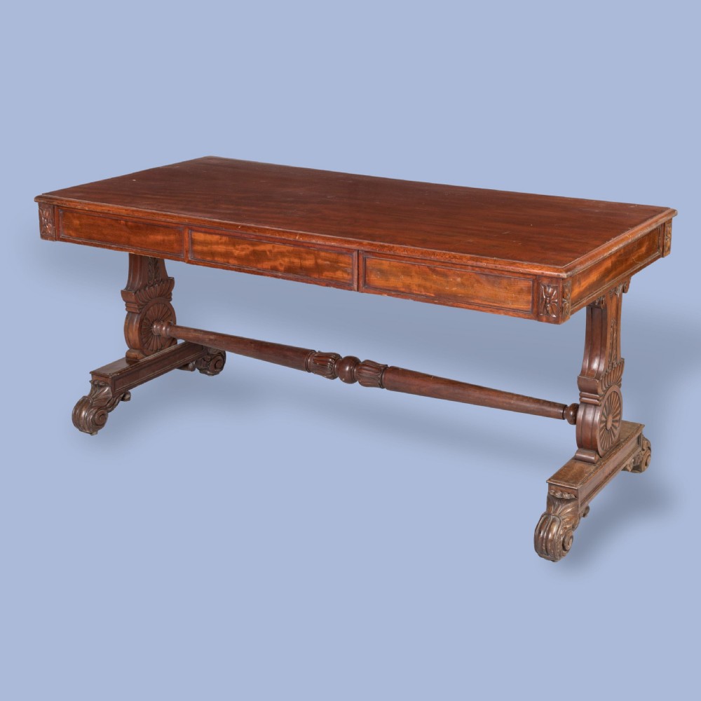 A Regency mahogany library table featuring a flat rectangular top, three frieze drawers, carved trestle end supports, and a central turned stretcher. View VI