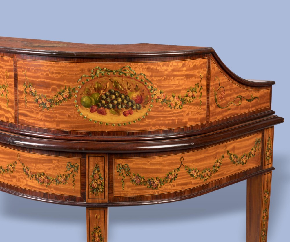 A hand-painted satinwood Carlton House desk featuring a curved superstructure of drawers, classical portrait medallions, floral swags, a leather writing surface, and square tapered legs on castors. View III