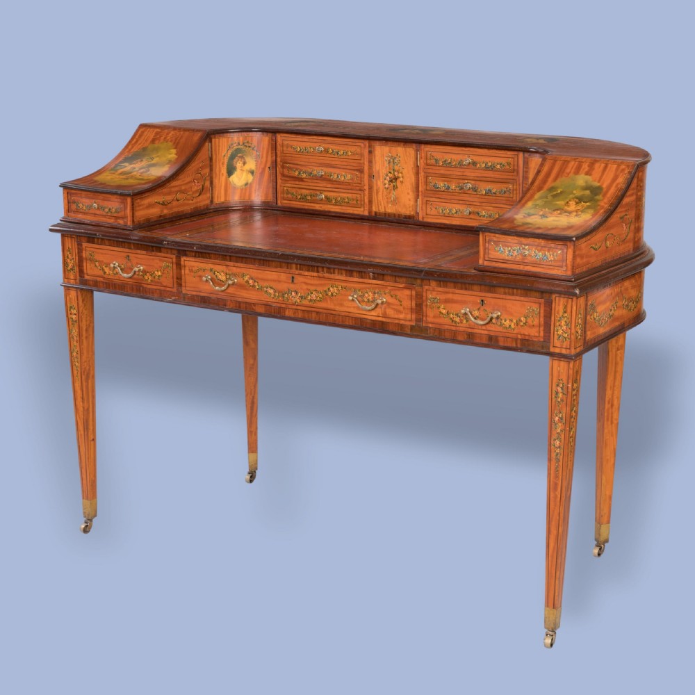 A hand-painted satinwood Carlton House desk featuring a curved superstructure of drawers, classical portrait medallions, floral swags, a leather writing surface, and square tapered legs on castors. View IX