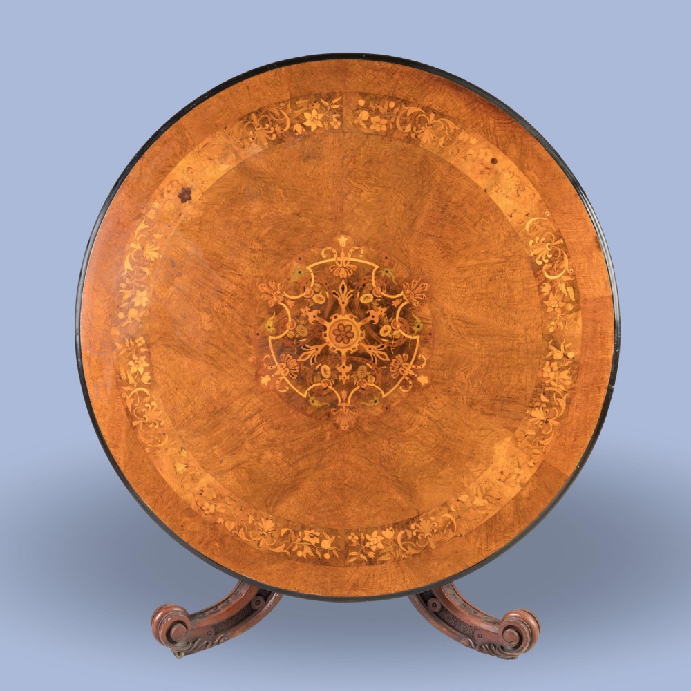An early Victorian circular centre table in warm brown walnut, featuring decorative floral marquetry inlays on top and an intricately carved scroll-foot pedestal base. View II