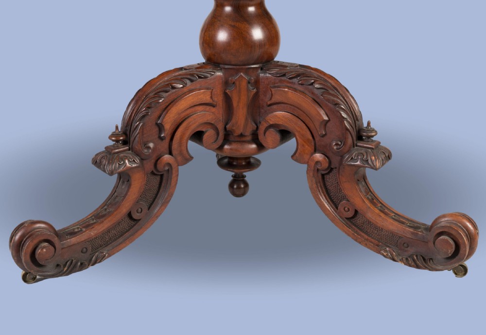 An early Victorian circular centre table in warm brown walnut, featuring decorative floral marquetry inlays on top and an intricately carved scroll-foot pedestal base. View V