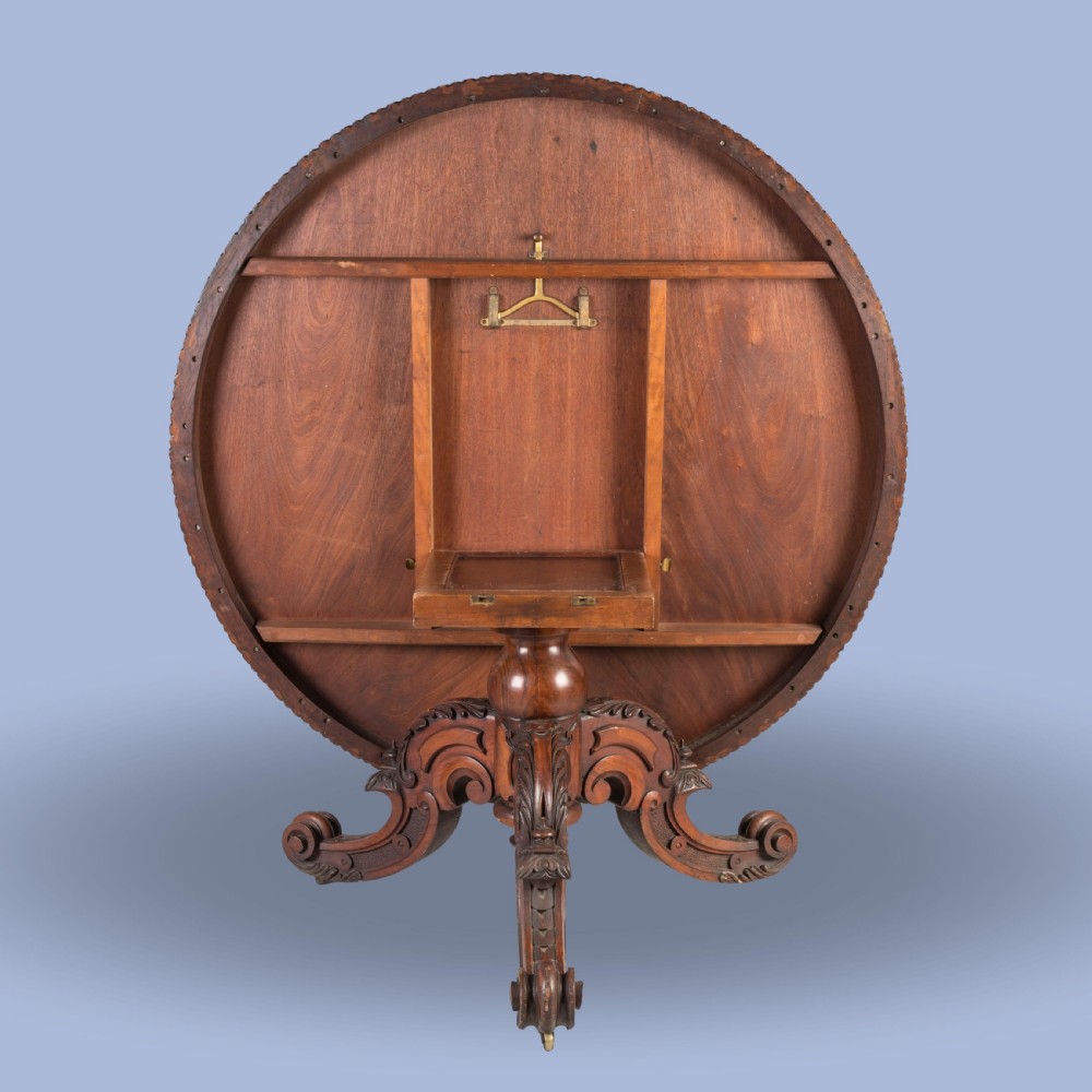 An early Victorian circular centre table in warm brown walnut, featuring decorative floral marquetry inlays on top and an intricately carved scroll-foot pedestal base. View VI