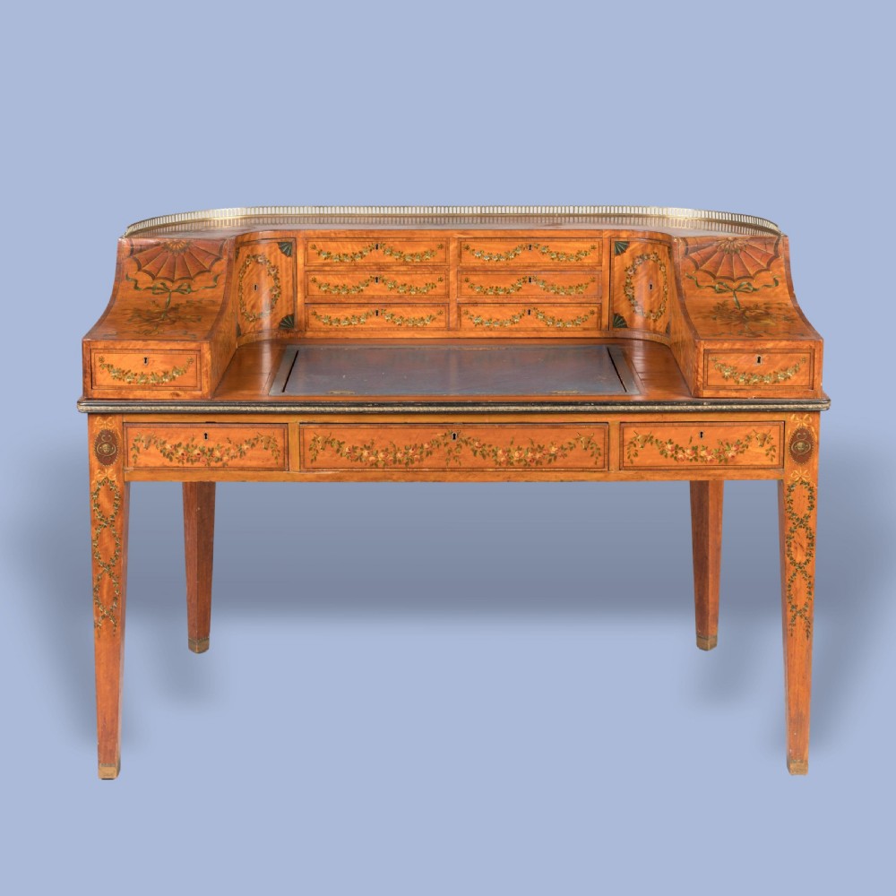 A satinwood Carlton House desk featuring hand-painted floral swags, a brass gallery rail, multiple superstructure drawers, and a central leather writing inset supported on square tapered legs. View II