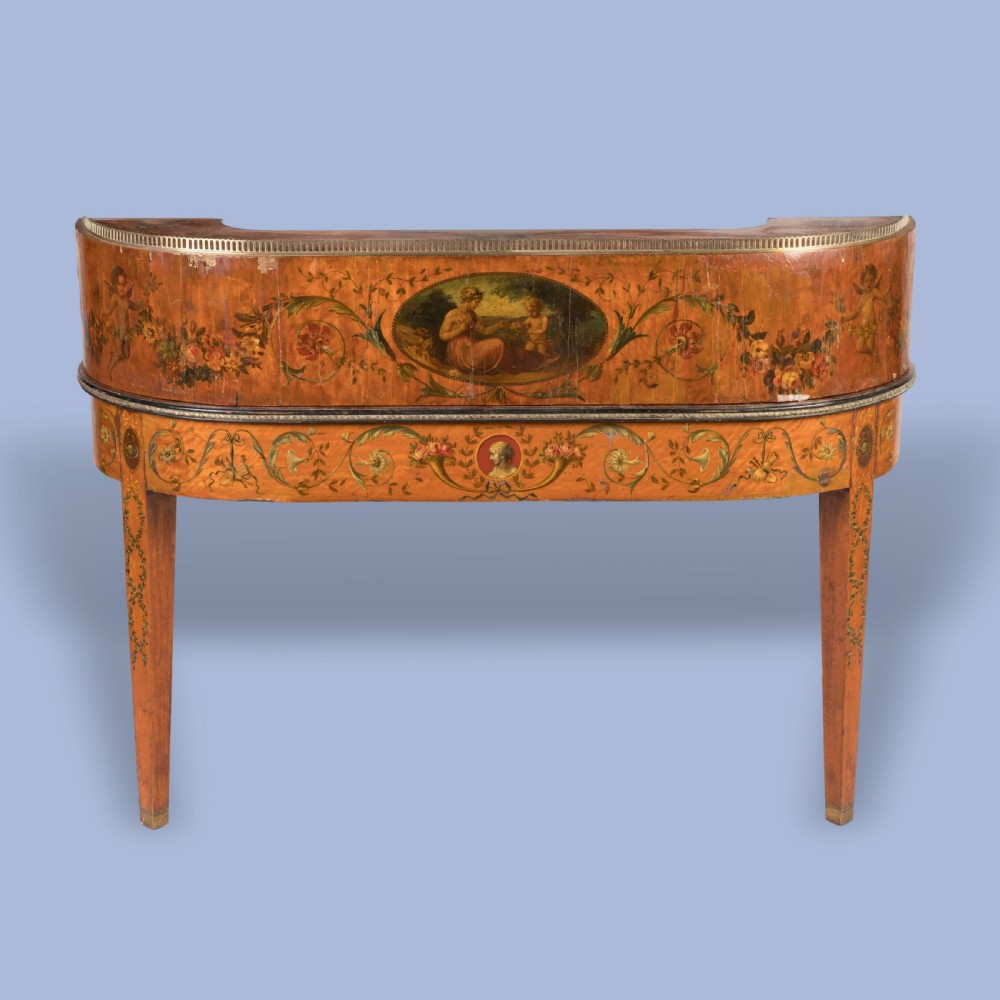 A satinwood Carlton House desk featuring hand-painted floral swags, a brass gallery rail, multiple superstructure drawers, and a central leather writing inset supported on square tapered legs. View V