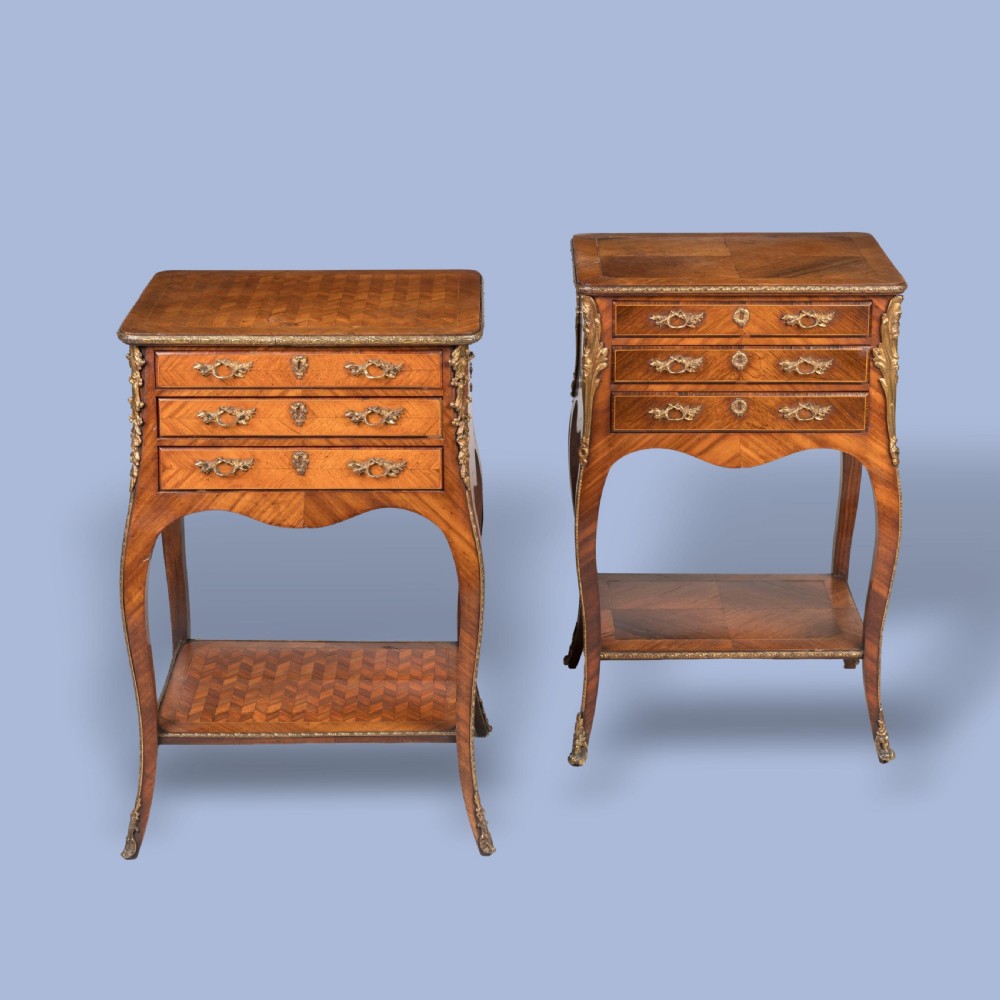 A matched pair of French Louis XV style wooden bedside tables featuring geometric parquetry veneer, three drawers, gilt bronze mounts, and slender cabriole legs.