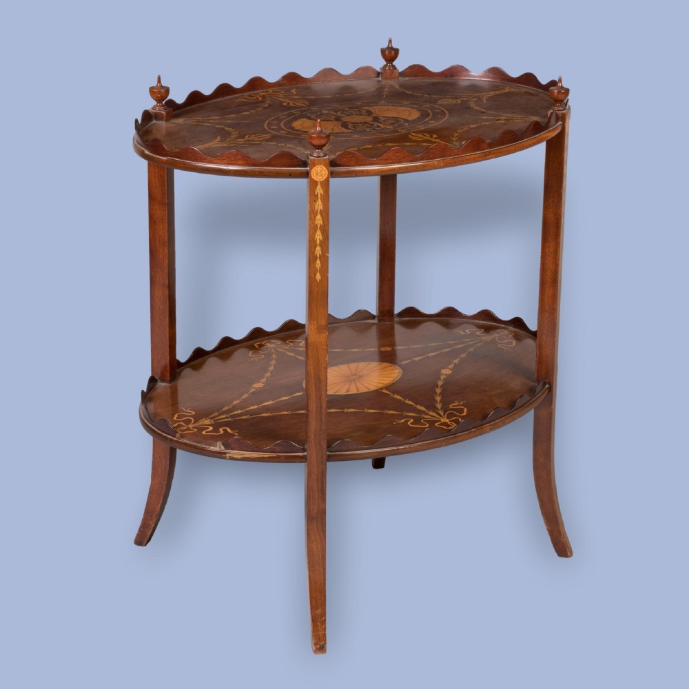 An Edwardian two-tier oval mahogany occasional table featuring scalloped galleried rims, urn finials, and detailed Neo-Classical marquetry inlays on turned legs.