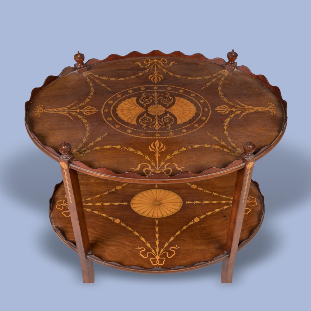 An Edwardian two-tier oval mahogany occasional table featuring scalloped galleried rims, urn finials, and detailed Neo-Classical marquetry inlays on turned legs. View III