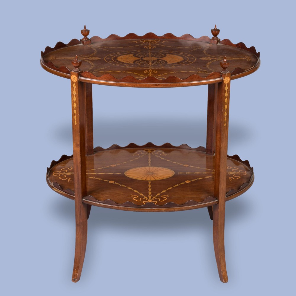 An Edwardian two-tier oval mahogany occasional table featuring scalloped galleried rims, urn finials, and detailed Neo-Classical marquetry inlays on turned legs. View IV