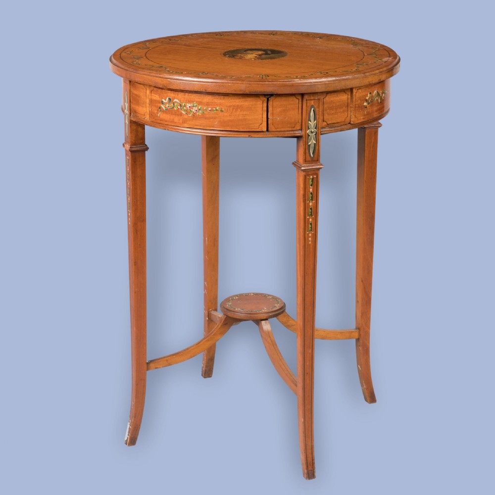 A round satinwood occasional table featuring hand-painted floral swags, tapered square legs, and a raised central stretcher.
