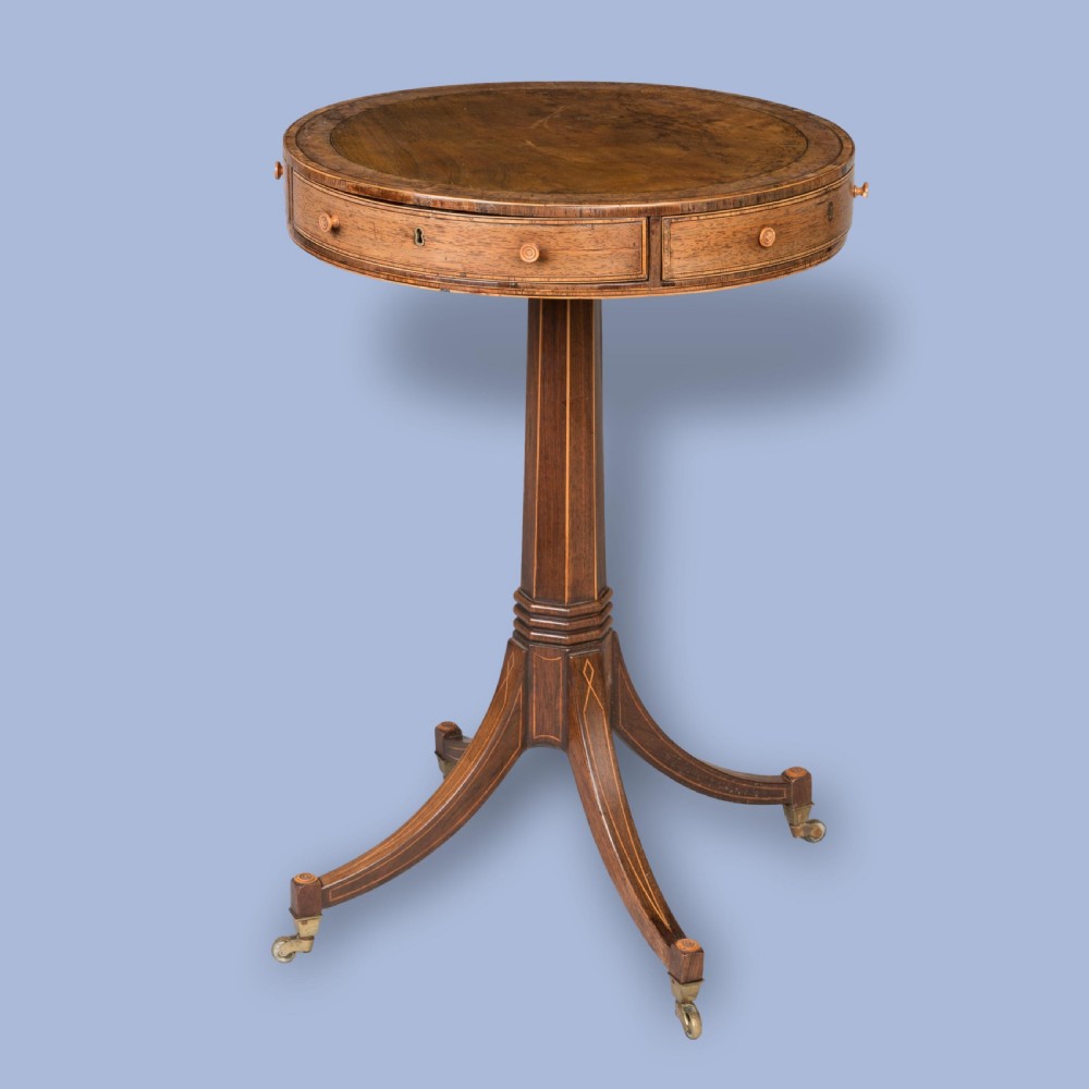 A small Regency mahogany drum table featuring a circular top with frieze drawers, supported on an inlaid central column and four swept legs with brass castors.