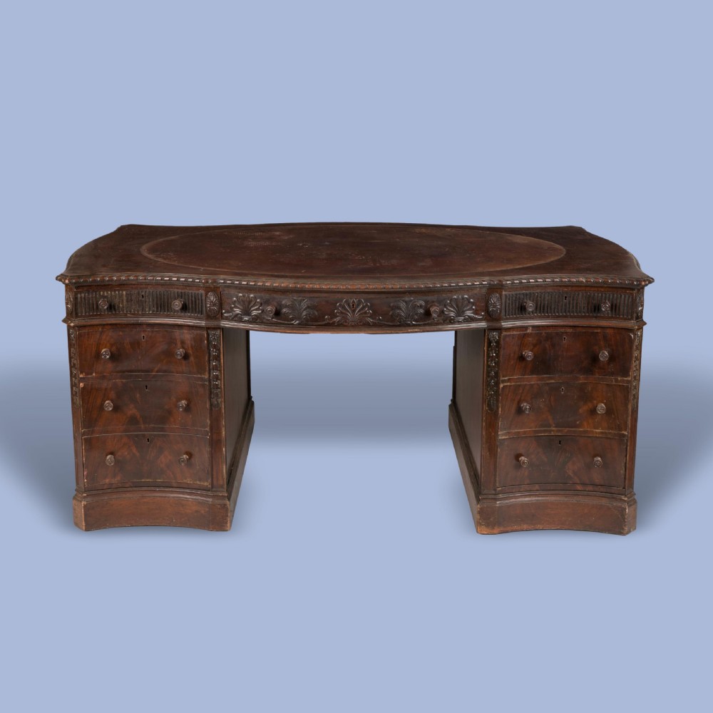 A dark mahogany serpentine pedestal desk featuring an oval leather-inset writing surface, carved foliate frieze, and twin drawer pedestals. View II