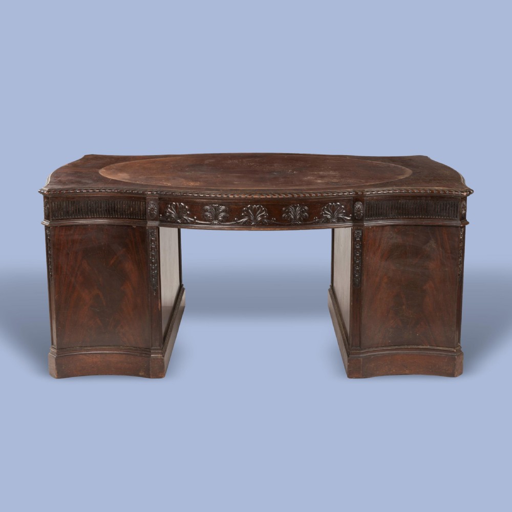 A dark mahogany serpentine pedestal desk featuring an oval leather-inset writing surface, carved foliate frieze, and twin drawer pedestals. View III