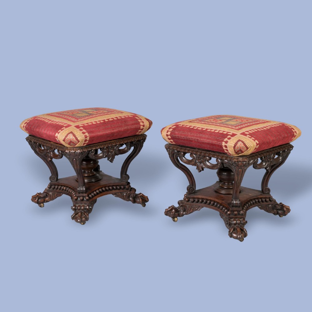 A pair of carved rosewood footstools with patterned red fabric cushions, scrolled supports, and claw feet.