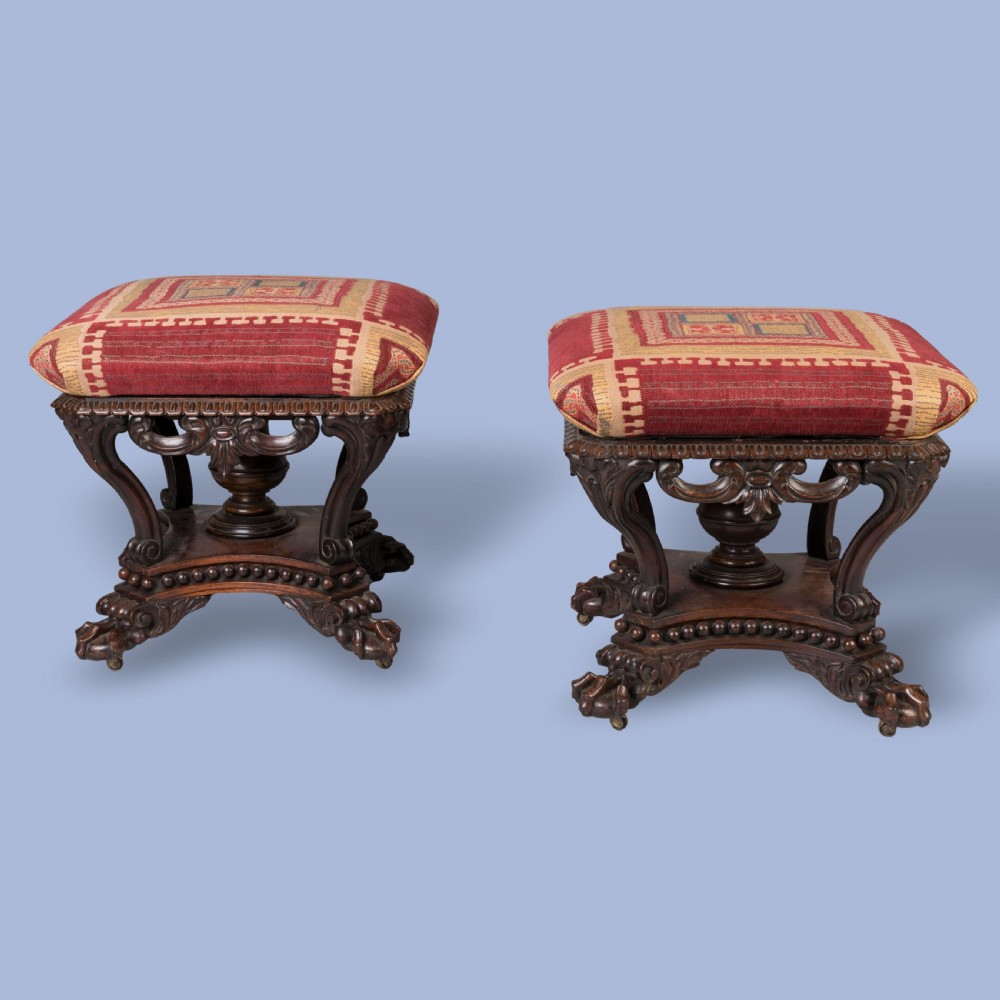A pair of carved rosewood footstools with patterned red fabric cushions, scrolled supports, and claw feet. View II