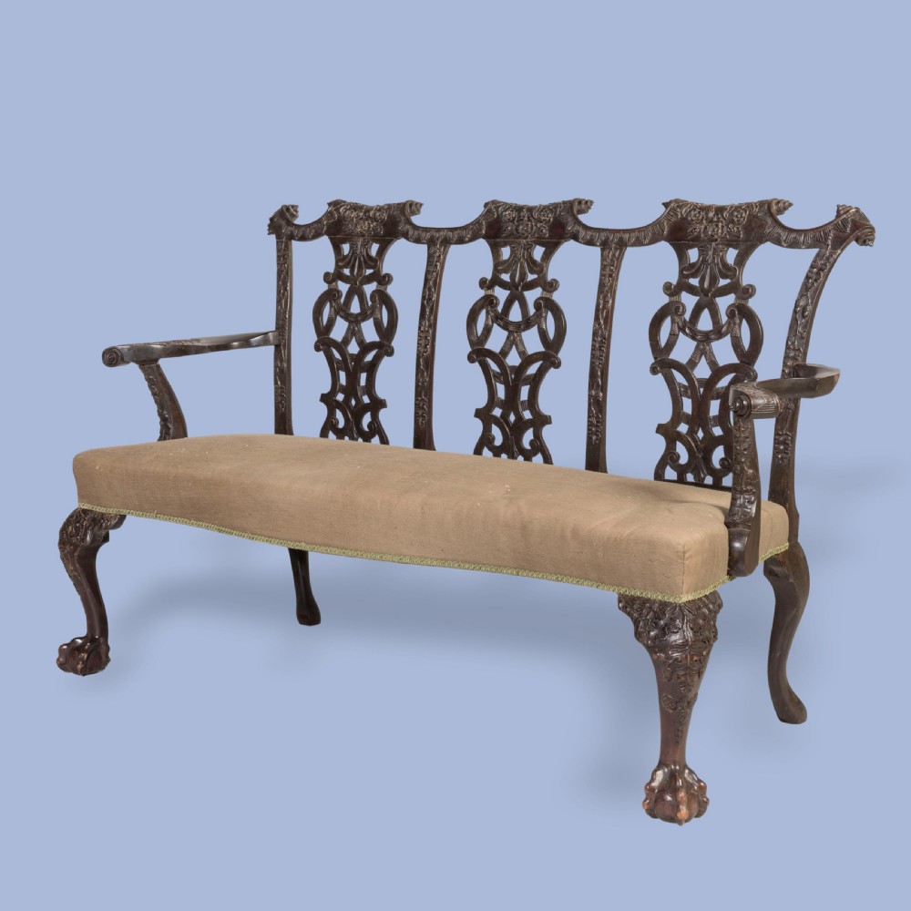 A Chippendale style dark mahogany triple chair-back settee featuring intricate pierced splats, carved cabriole legs, ball-and-claw feet, and a beige upholstered seat. View II