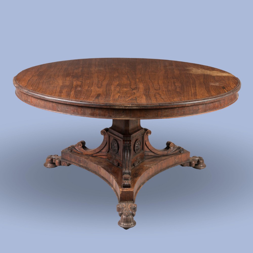 A circular 19th-century William IV centre table crafted from dark wood with a carved central pedestal and platform base with scroll feet.