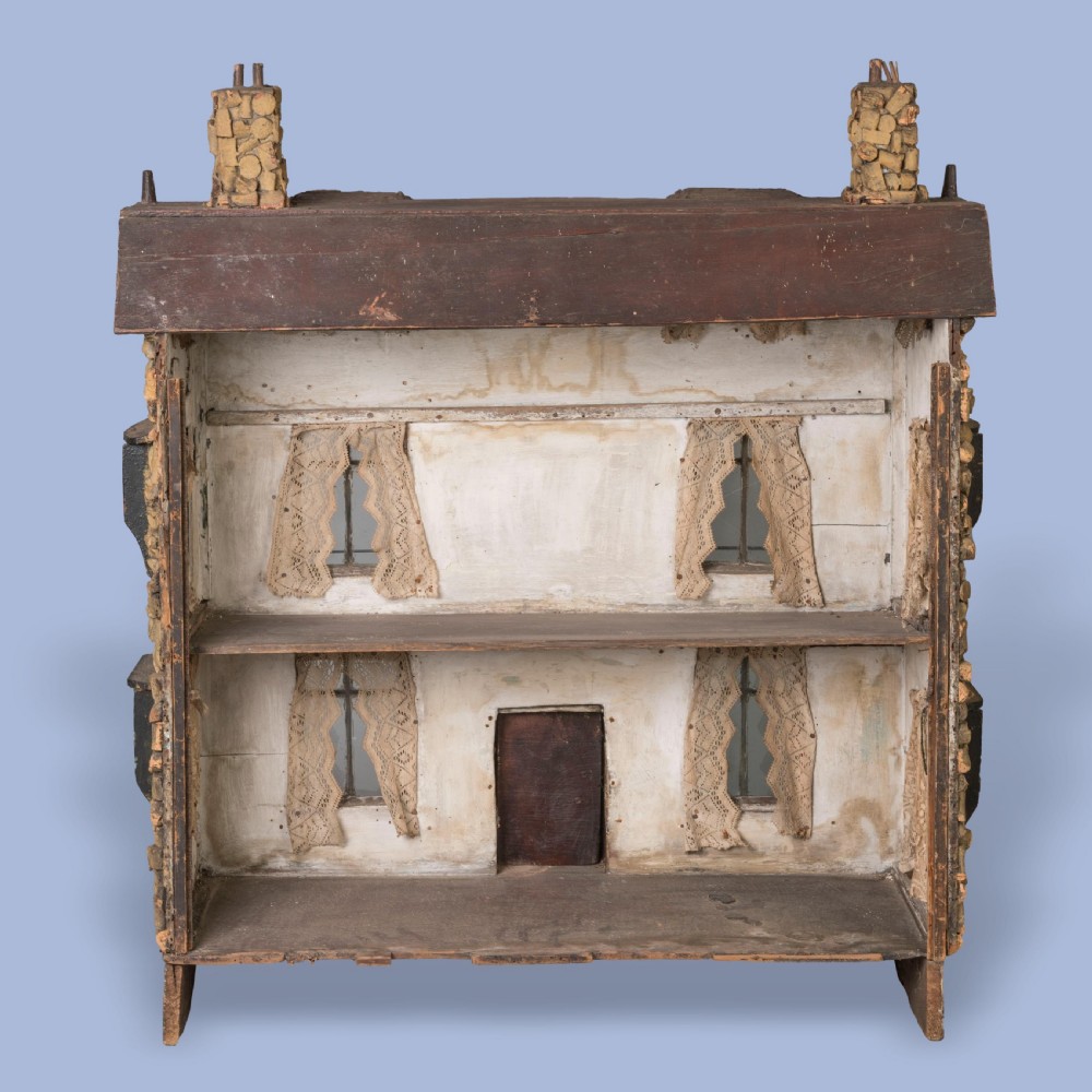 A miniature two-storey detached house constructed from wine corks and wood, featuring gables, glazed windows with lace curtains, classical medallion reliefs, and a base decorated with embedded seashells. View IV