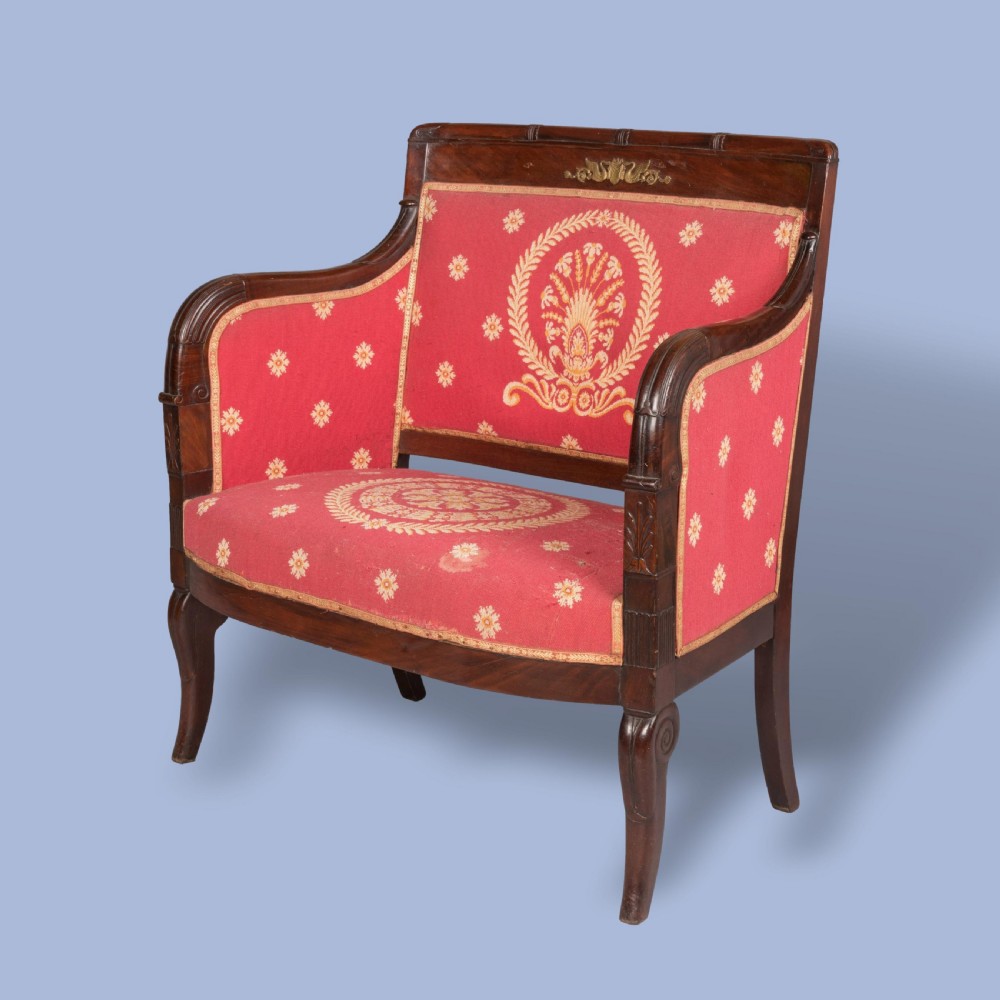 An Empire style dark mahogany fauteuil armchair upholstered in crimson patterned textile with gilt metal crest mounts.