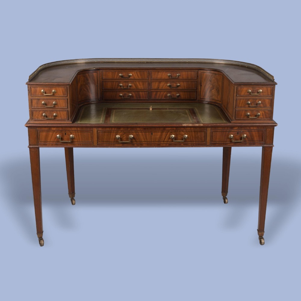 A mahogany Carlton House desk featuring a wrap-around drawer superstructure, brass gallery railing, green leather writing surface, and tapered legs on castors. View II