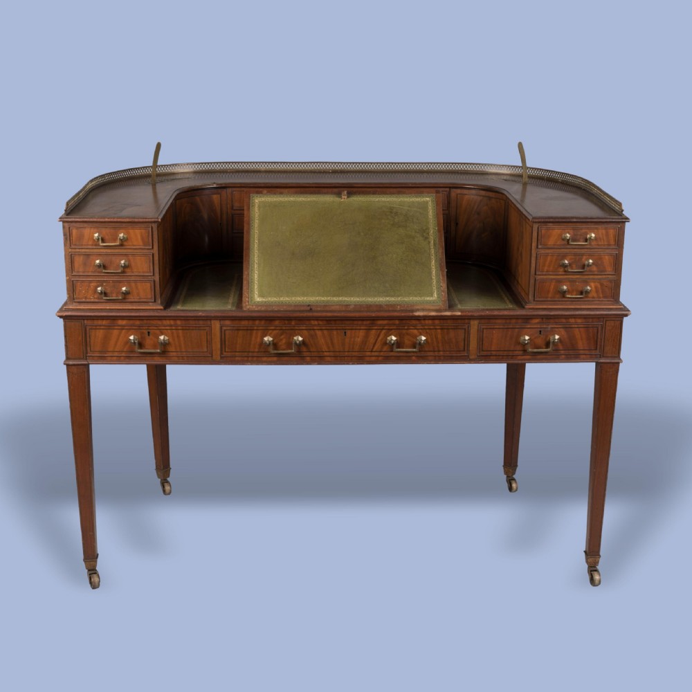 A mahogany Carlton House desk featuring a wrap-around drawer superstructure, brass gallery railing, green leather writing surface, and tapered legs on castors. View III