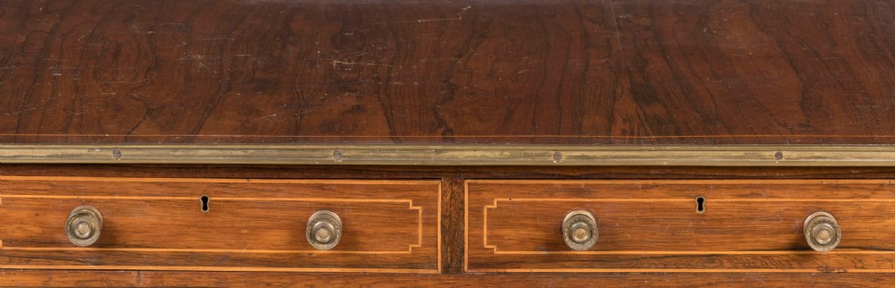 A Regency rosewood sofa table featuring drop leaves, two frieze drawers with brass knobs, brass edging, turned supports, and splayed legs ending in brass lion paw castors. View III